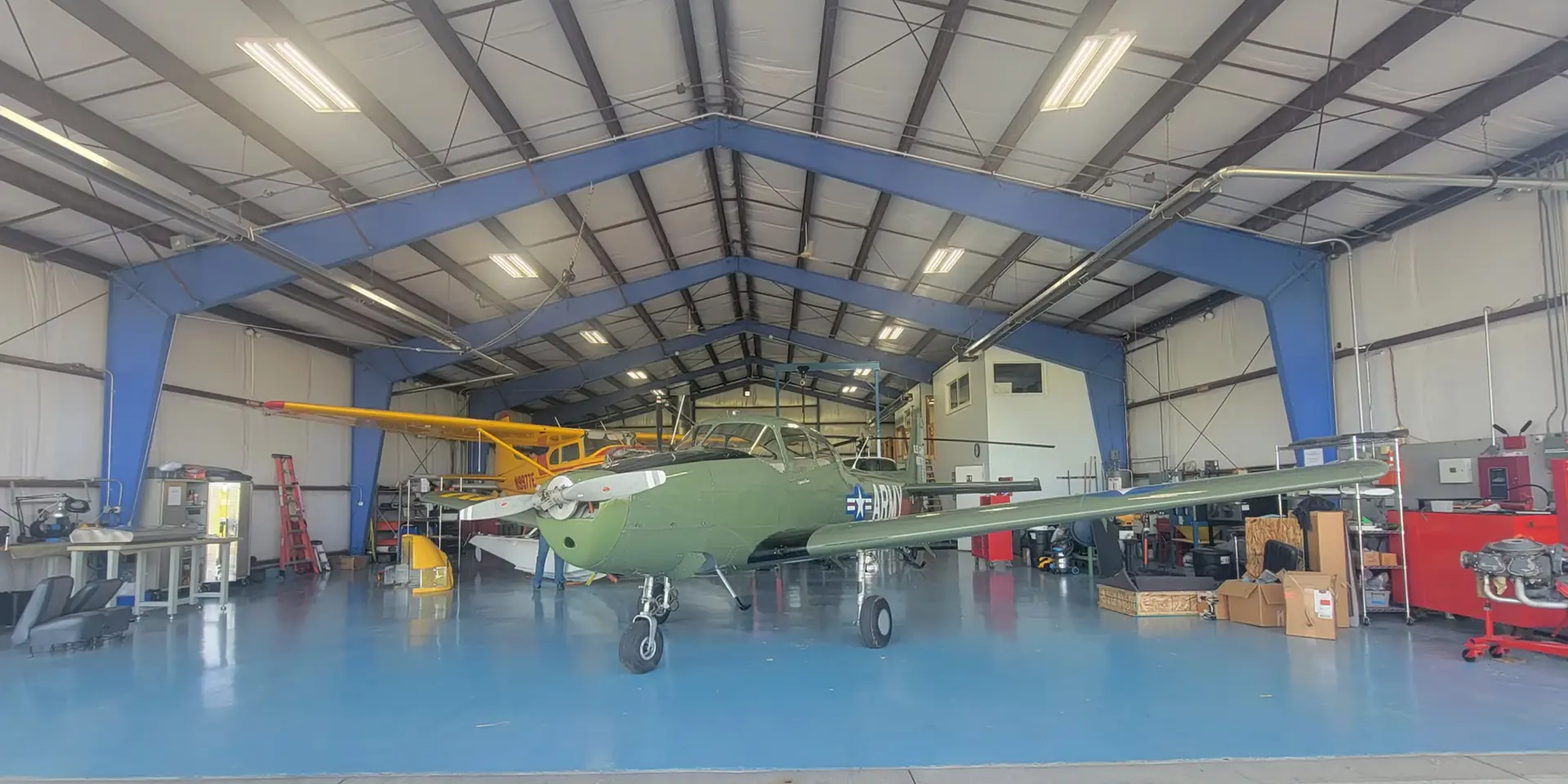 Precision Aviation maintenance hangar with a vintage green military-style aircraft and yellow helicopter under restoration